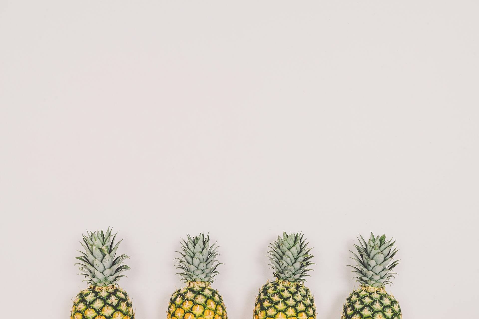 A row of pineapples against a white wall.